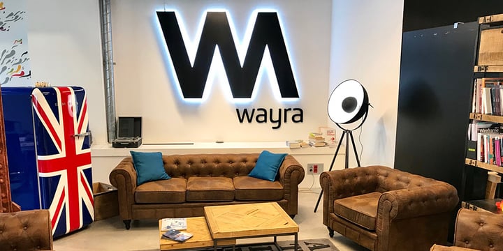 Two brown sofas in an office around a coffee table. There is a Wayra logo in the background.
