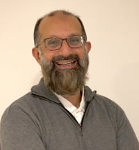 Image of CFO. Middle-aged, Middle-Eastern man with a beard, wearing classes smiling.