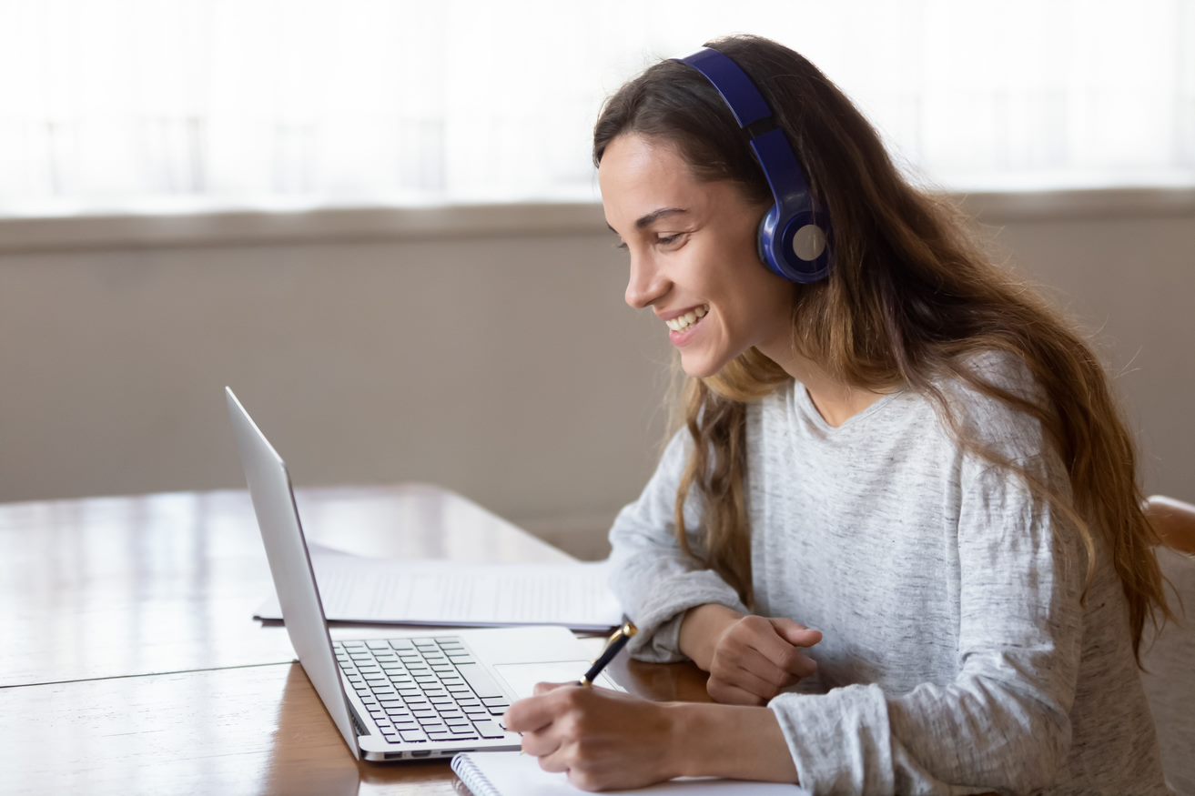 Cheerful young Caucasian woman looking a computer laptop with headphone on ears.