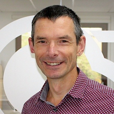 Middle aged Caucasian man smiling - wearing a white spotted shirt.