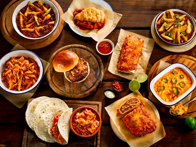 A variety of fast food is displayed on a table, including burger, pasta, lasagne, sauces and more 