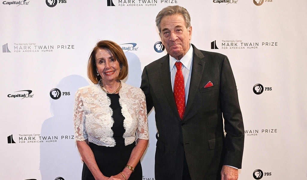 Nancy Pelosi and her husband Paul are standing together, both are dressed in black matched with red and white