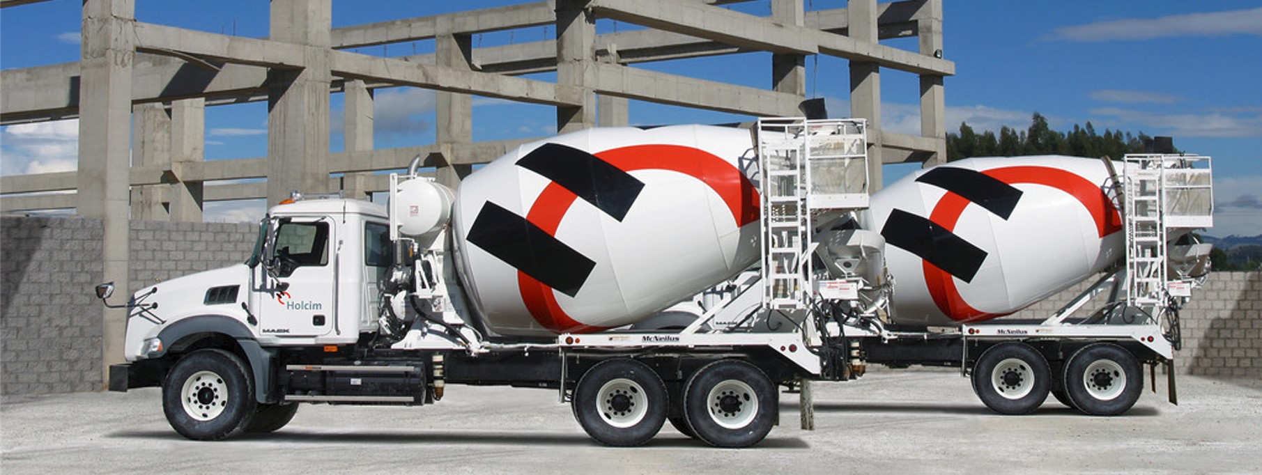 Two concrete mixer trucks of Holcim Inc parked besides a construction site.