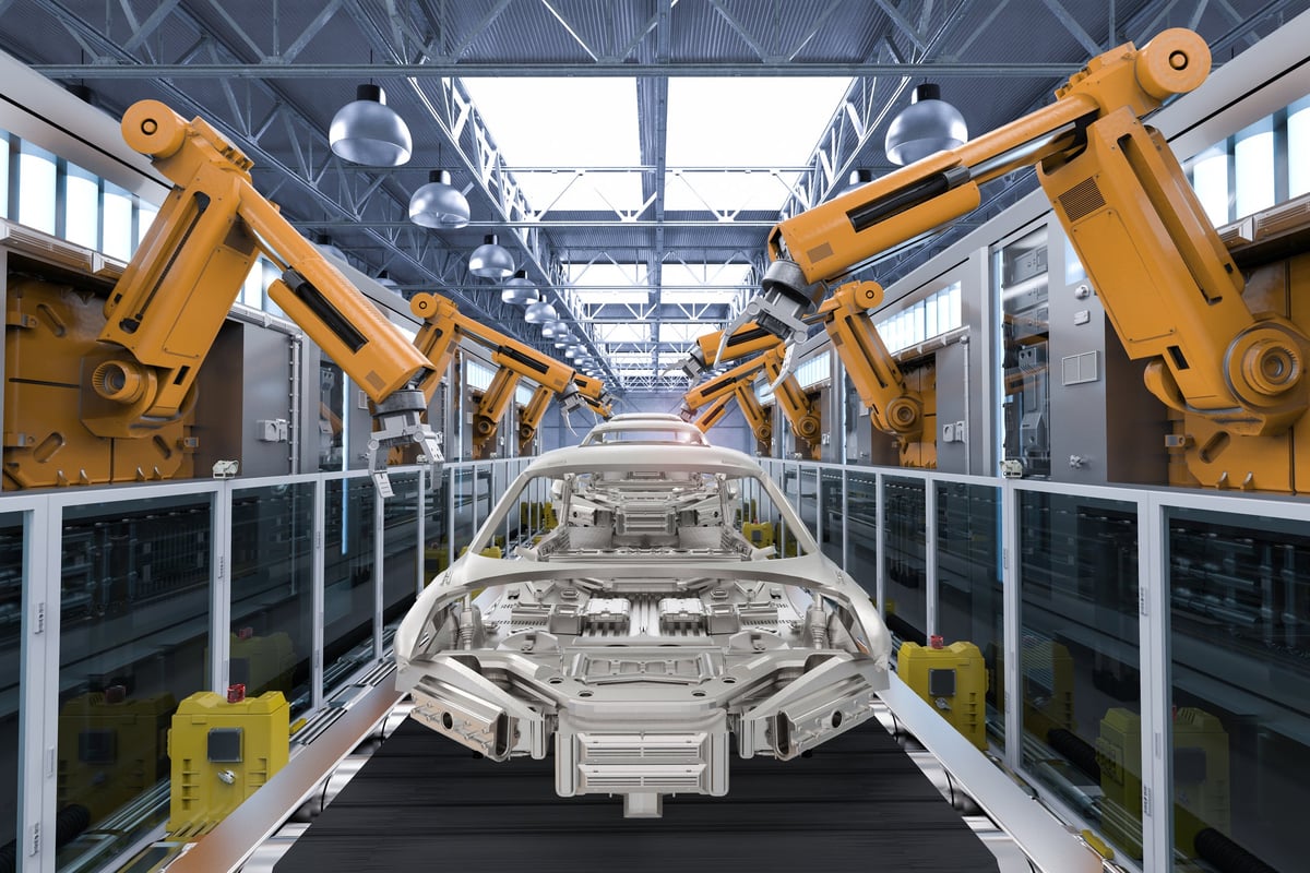 The structure of a car moves along a conveyer belt with robotic cranes on either side to attach additional parts.
