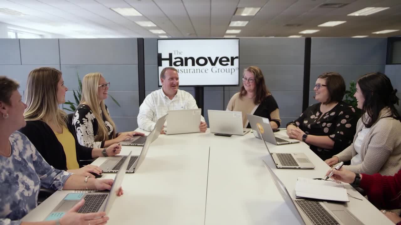 Multiple Hanover Insurance Inc employees are having meeting in the company's conference room, each holding laptops.