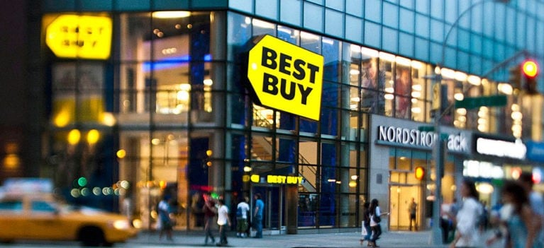 On a glass building located in a busy thoroughfare, the Best Buy Co Inc emblem is displayed in black and yellow
