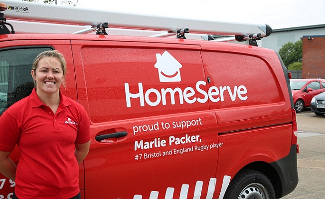An employee of HomeServe standing in front of the company bus wearing a red T-shirt with the company logo.