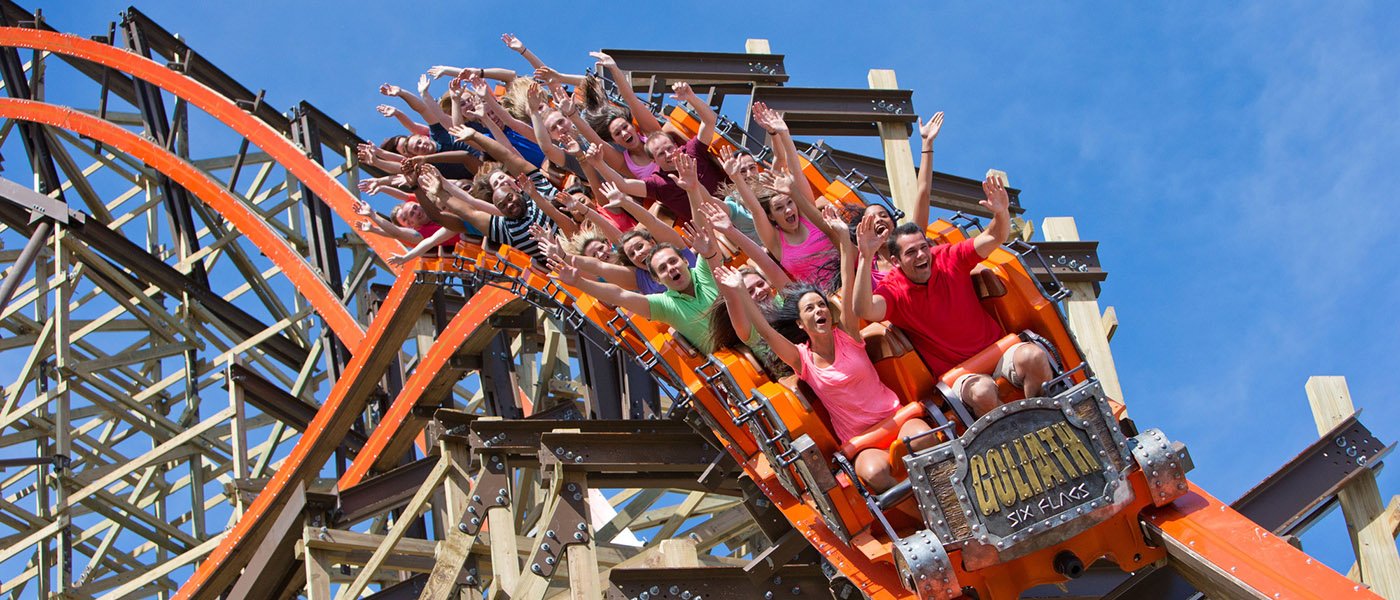 Many people are enjoying a wooden coaster ride named Goliath  in a Six Flags Entertainment Park.
