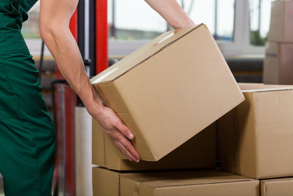 Hands of warehouse worker lifting box, horizontal