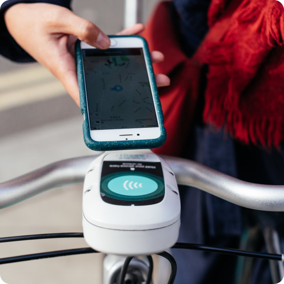A close-up of a human hand using the Beryl app to rent the Beryl bike. A contactless rental by holding the phone near the reader on the bike.