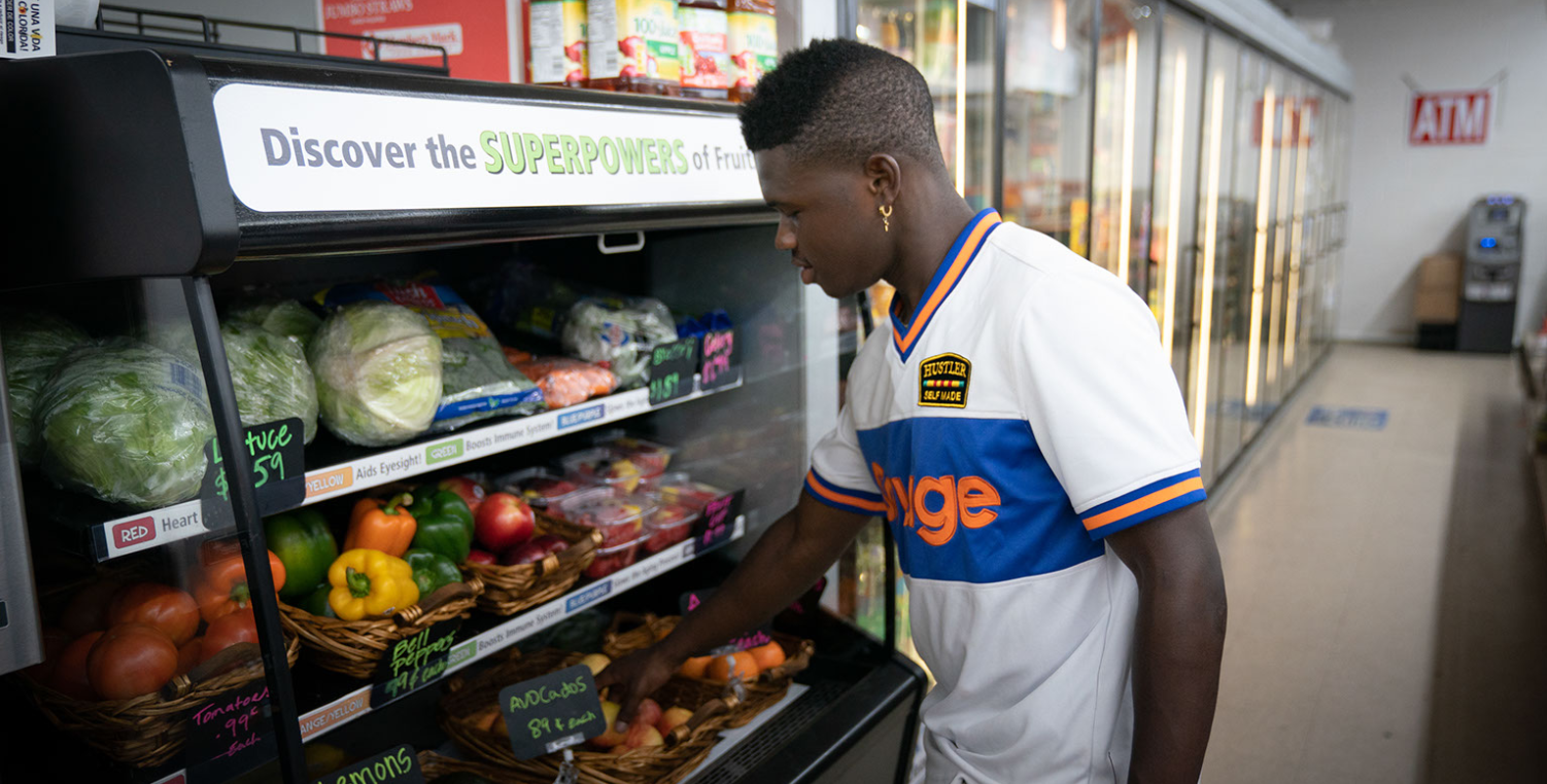 you man selecting produce from display case at corner store