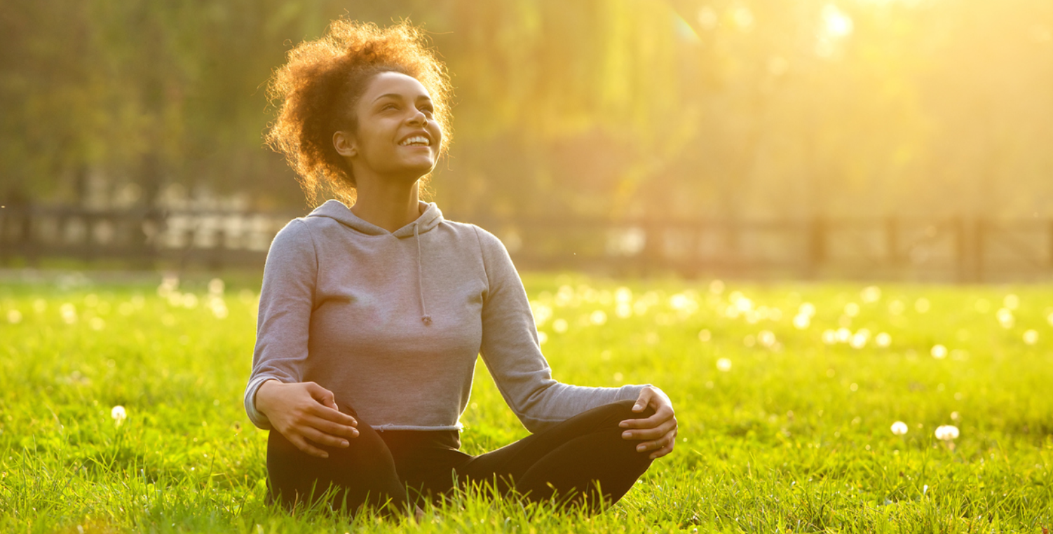 smiling woman sitting in yoga pose in field