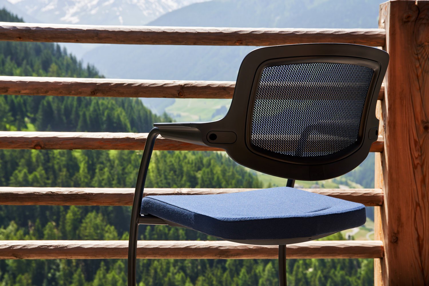 close up of blue giroflex 161 visitor chair with a wooden railing behind it, with mountain forests in the background