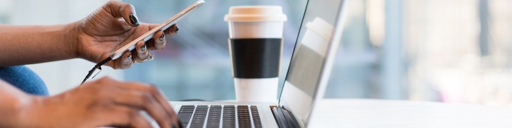 Female hand using her phone and laptop with a cup of coffee