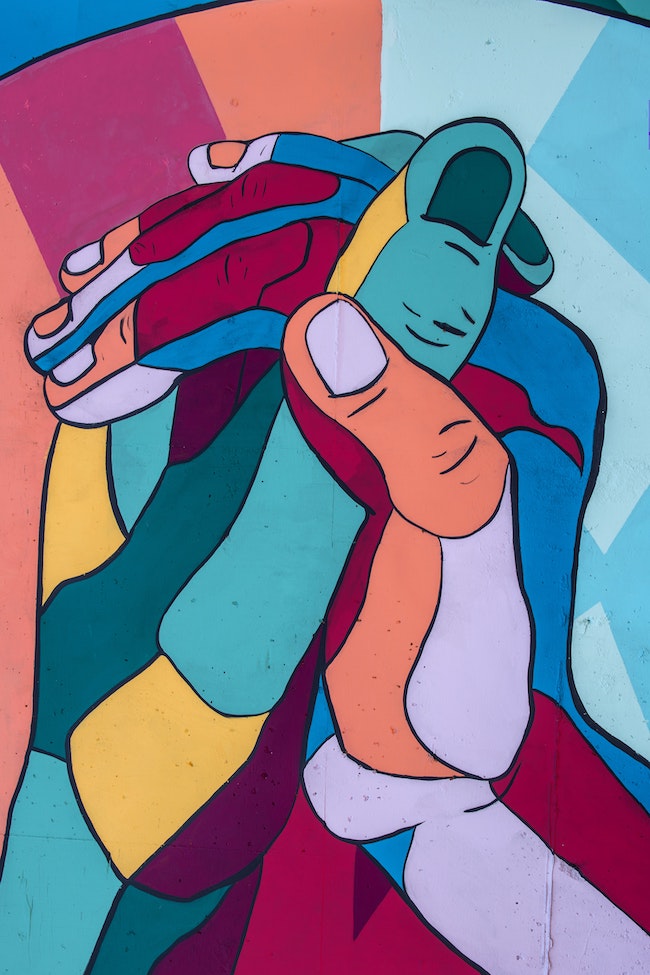 A painting of two multicolored hands clasp one another, diversity, equity, inclusion