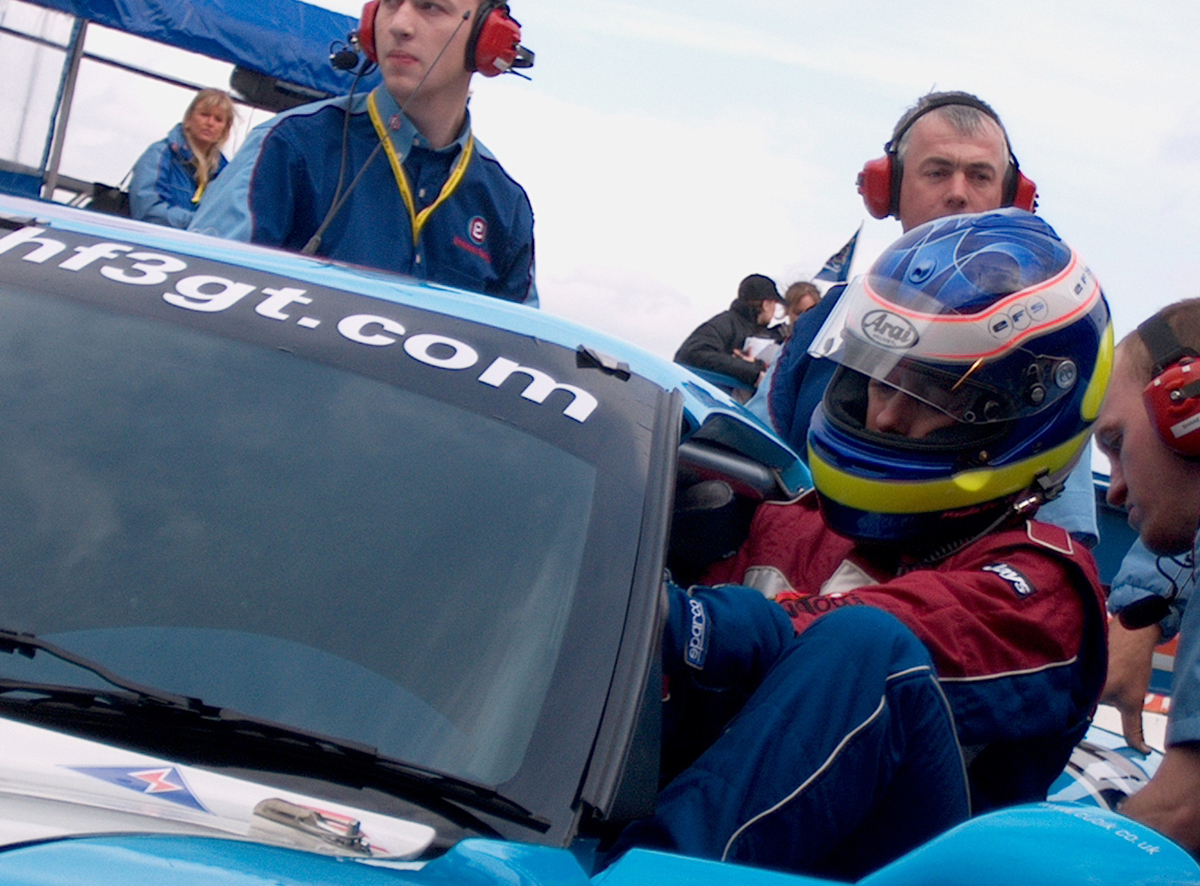 Conducteur de voiture de course entrant dans une voiture avec l'équipage des stands portant des casques autour d'eux