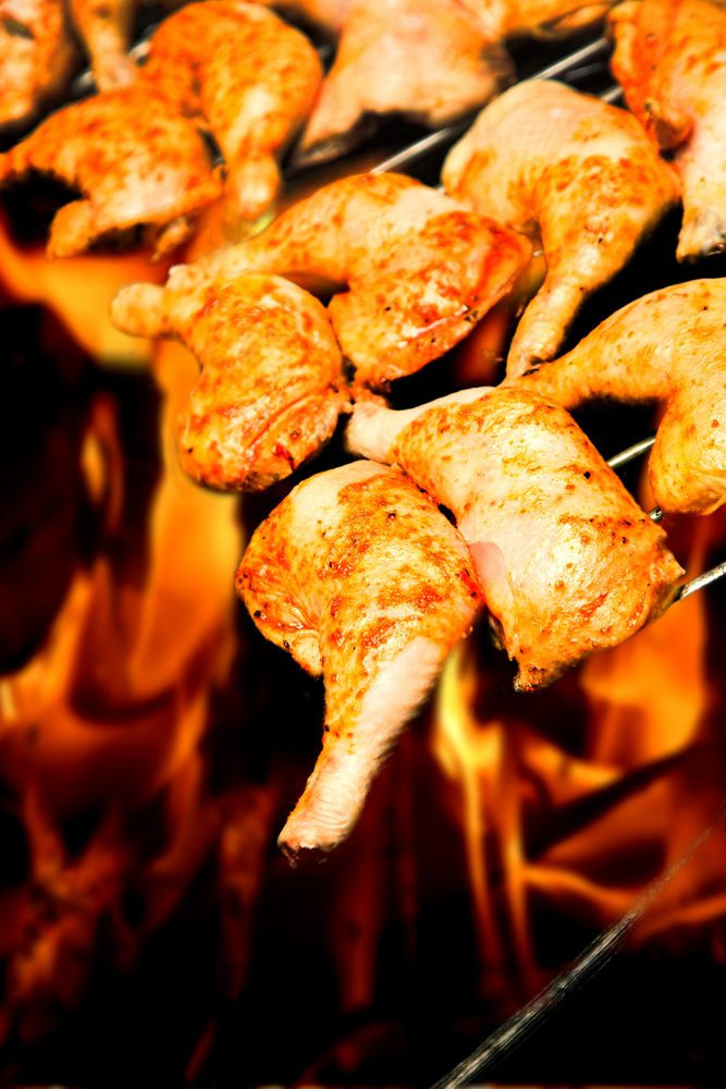 chicken pieces on a bbq with fire behind them