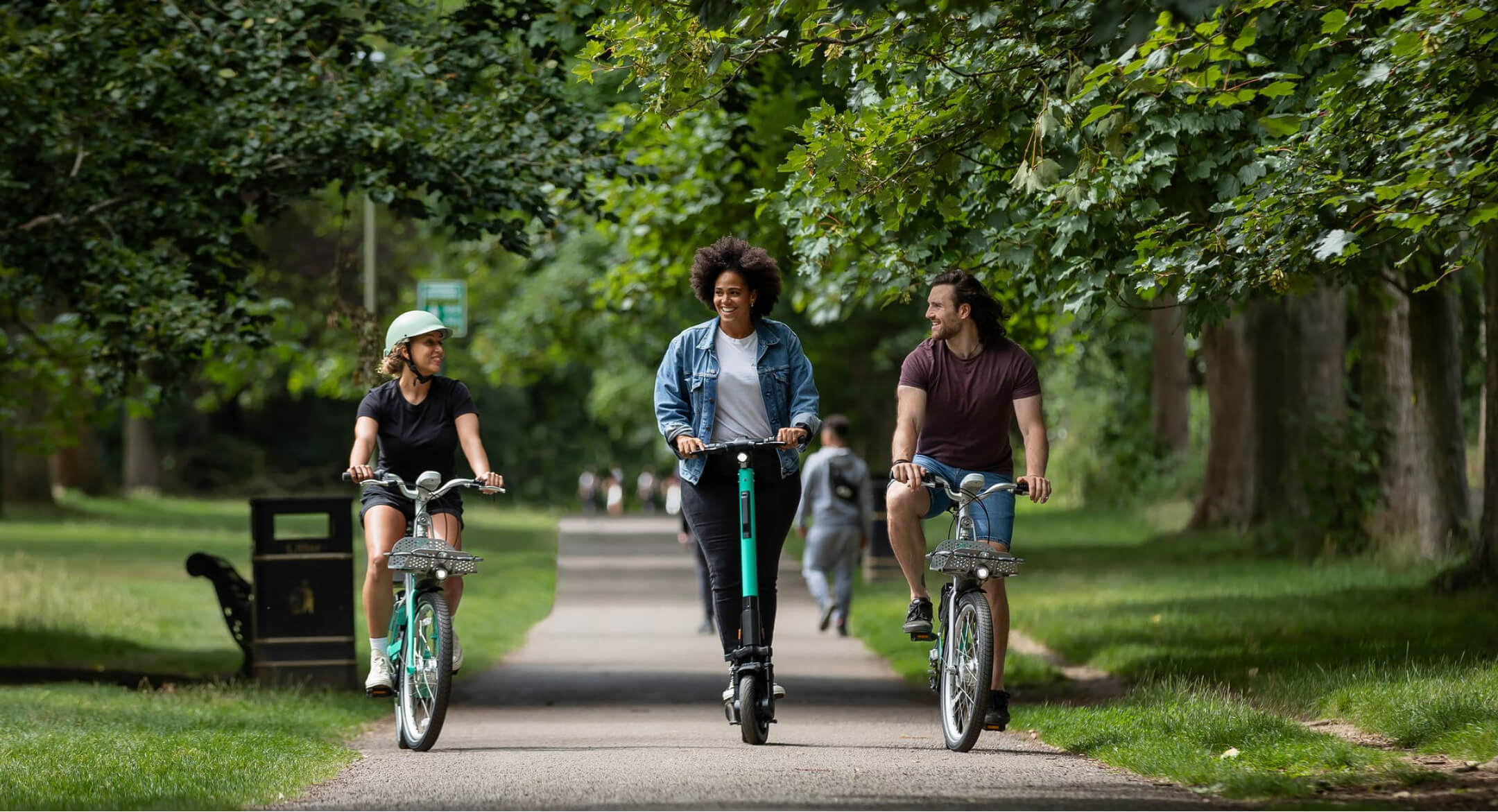 A wide shot of 3 people riding through a park. Two of them are on Beryl bikes; one is riding a Beryl scooter.