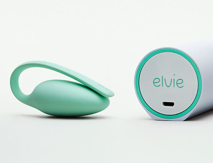 A product photo against a grey background. Elvie Trainer (hardware device) next to a box with a charger.