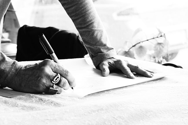 Black and white image of someone writing on a piece of paper leaning on a desk