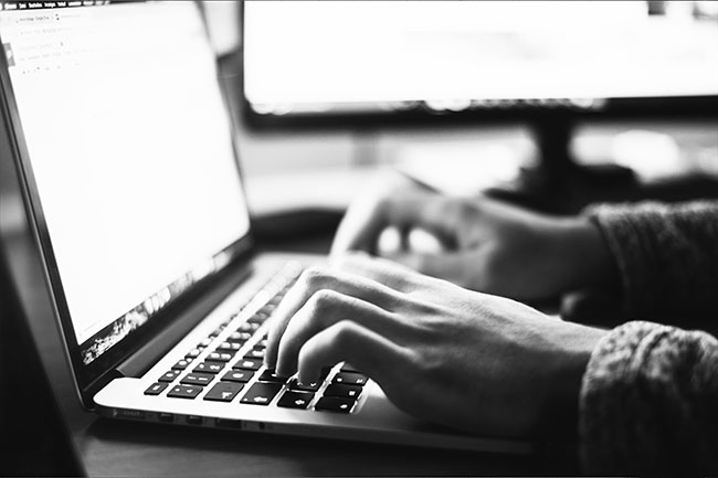 Black and white photo of someone writing on a laptop keyboard. 