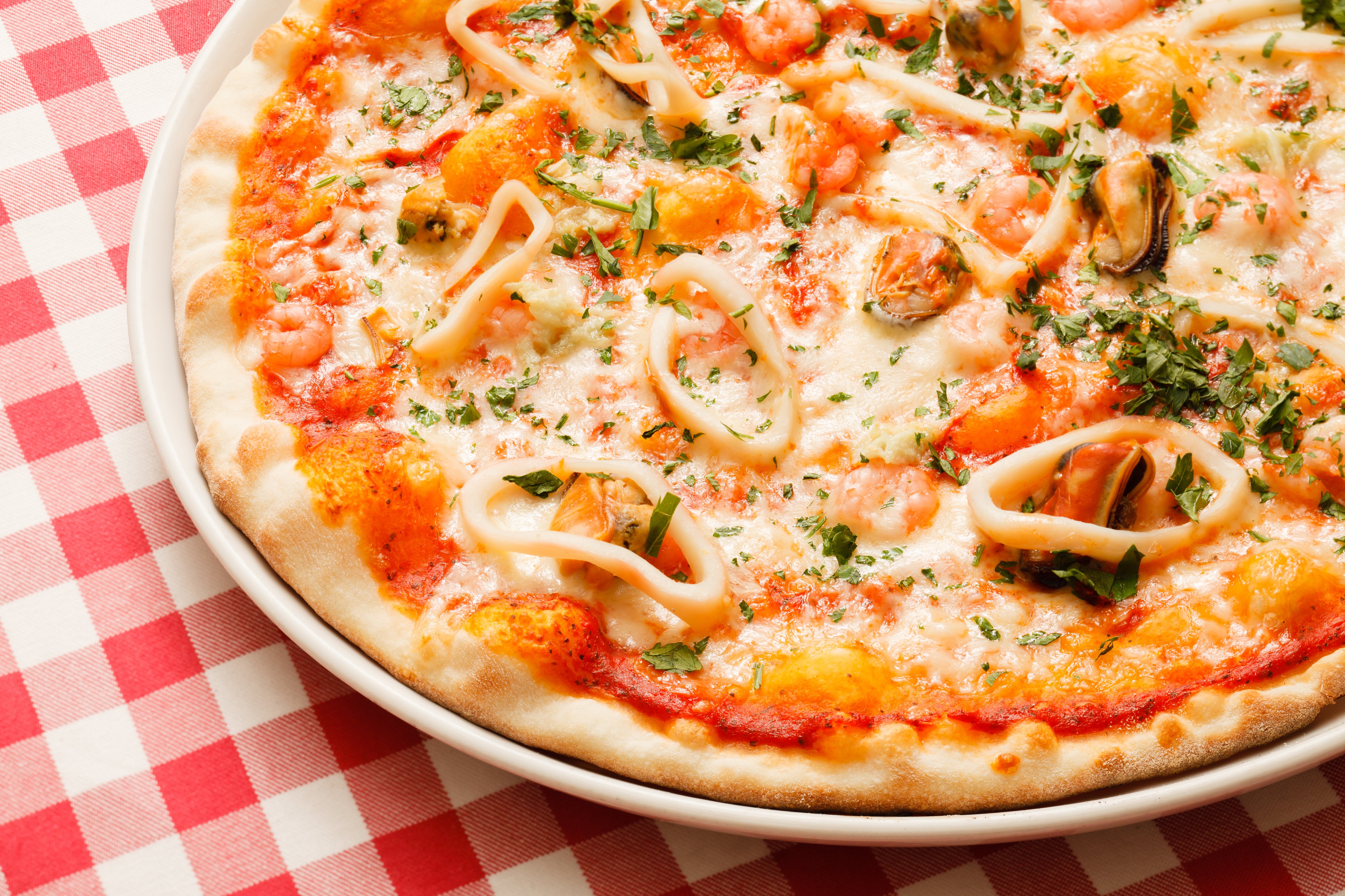 A pizza with calamari rings sits on a red checkered tablecloth