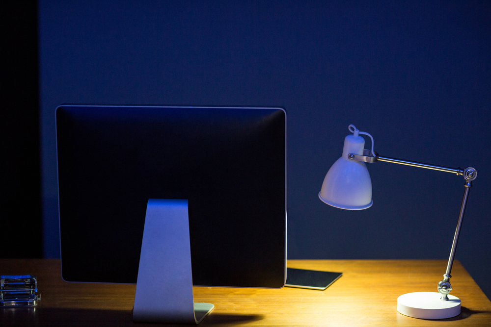 Close-up computer monitor and illuminated lamp on office desk at night