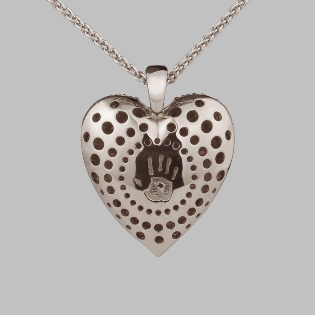 A white gold necklace in the shape of a heart, back view with a concentric pattern of holes and the Stephen Einhorn hand print logo in the middle