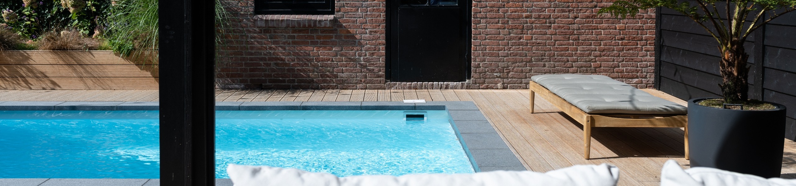 Maatwerk skimmerzwembad buiten met schuur van steen zicht vanuit houten poolhouse op zwembad met houten vlonder