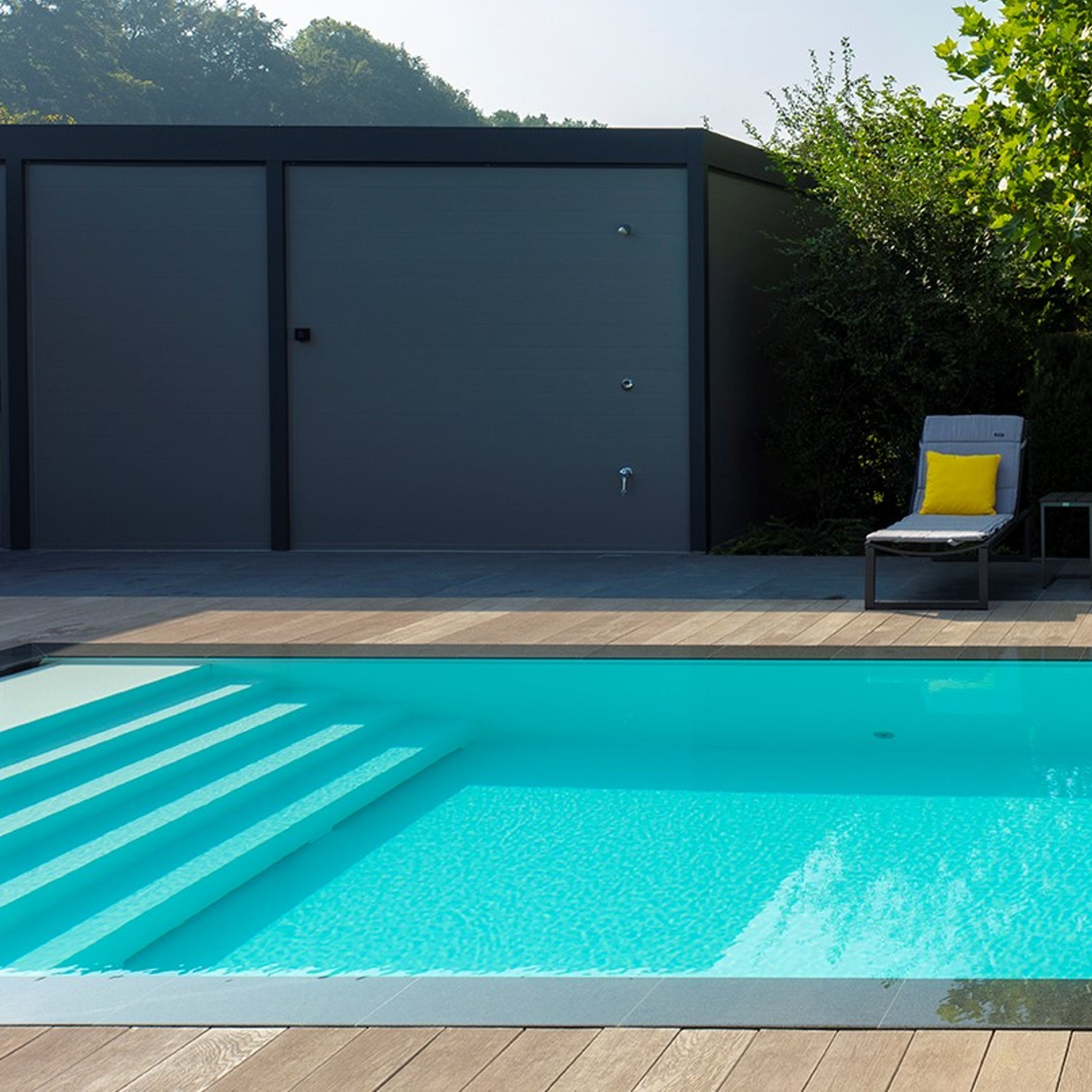 Loungetrap in een overloopzwembad met houten vlonder eromheen een poolhouse en loungestoel