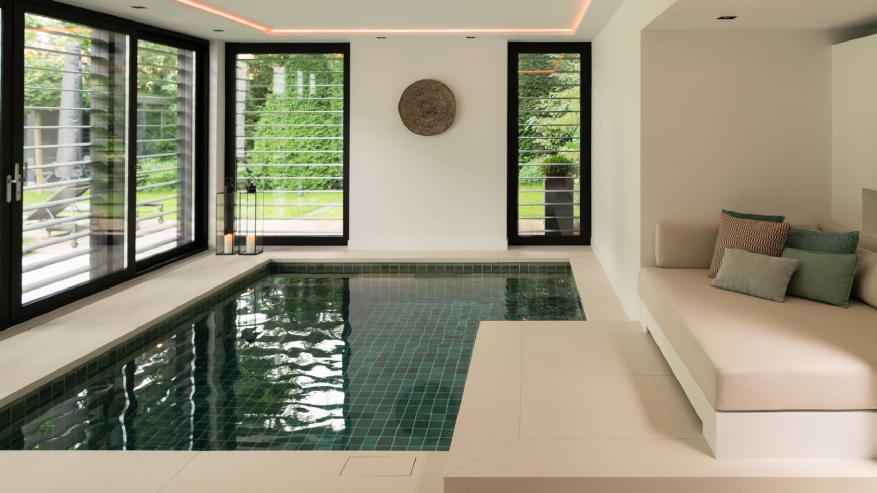 Bouwkundige plunge pool binnenzwembad groenblauwe tegels met lounge ernaast en grote ramen met zwarte kozijnen