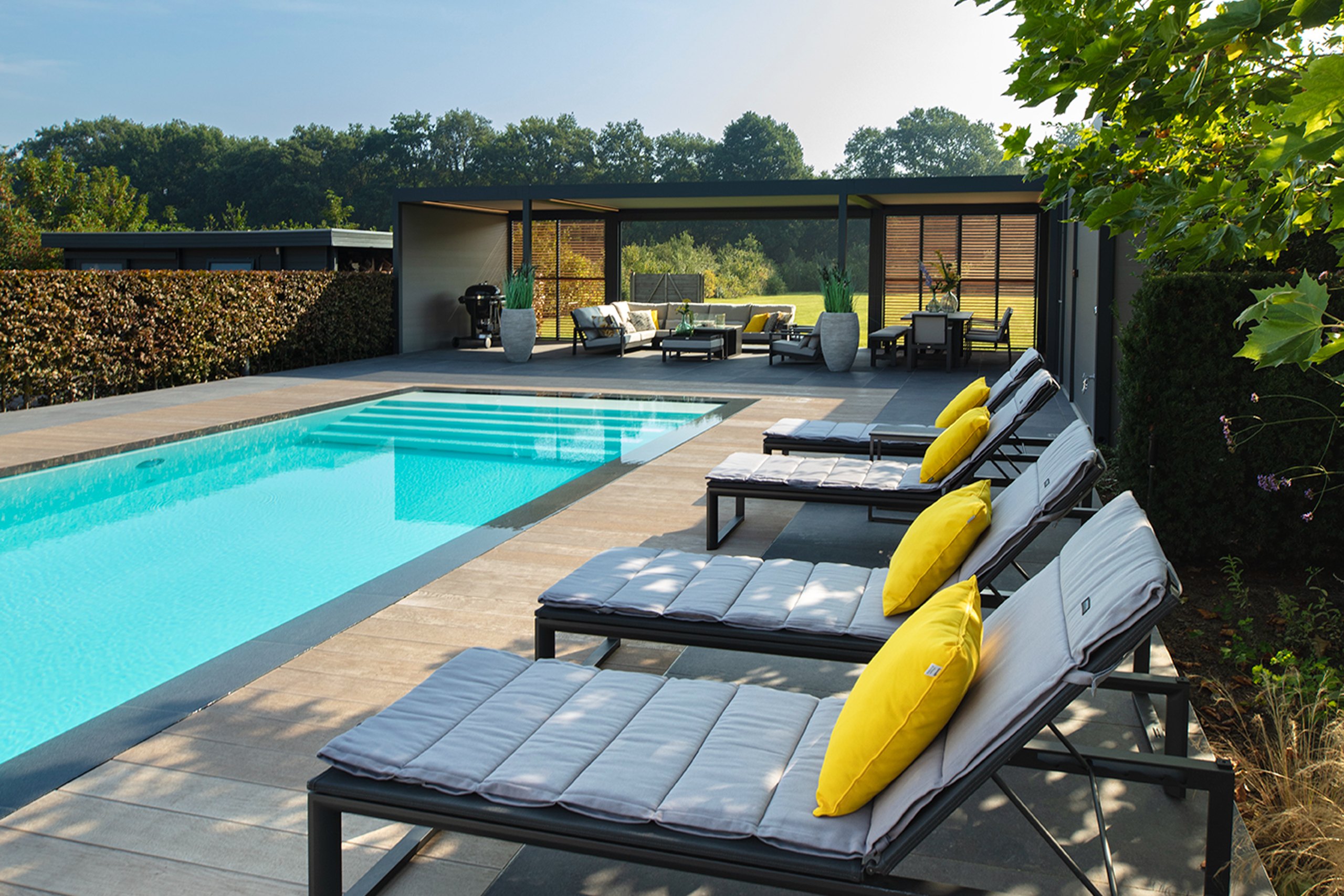 Overloopzwembad infinity pool van starline met ruim poolhouse en vier ligbedden met geel kussen langs de zwembadrand