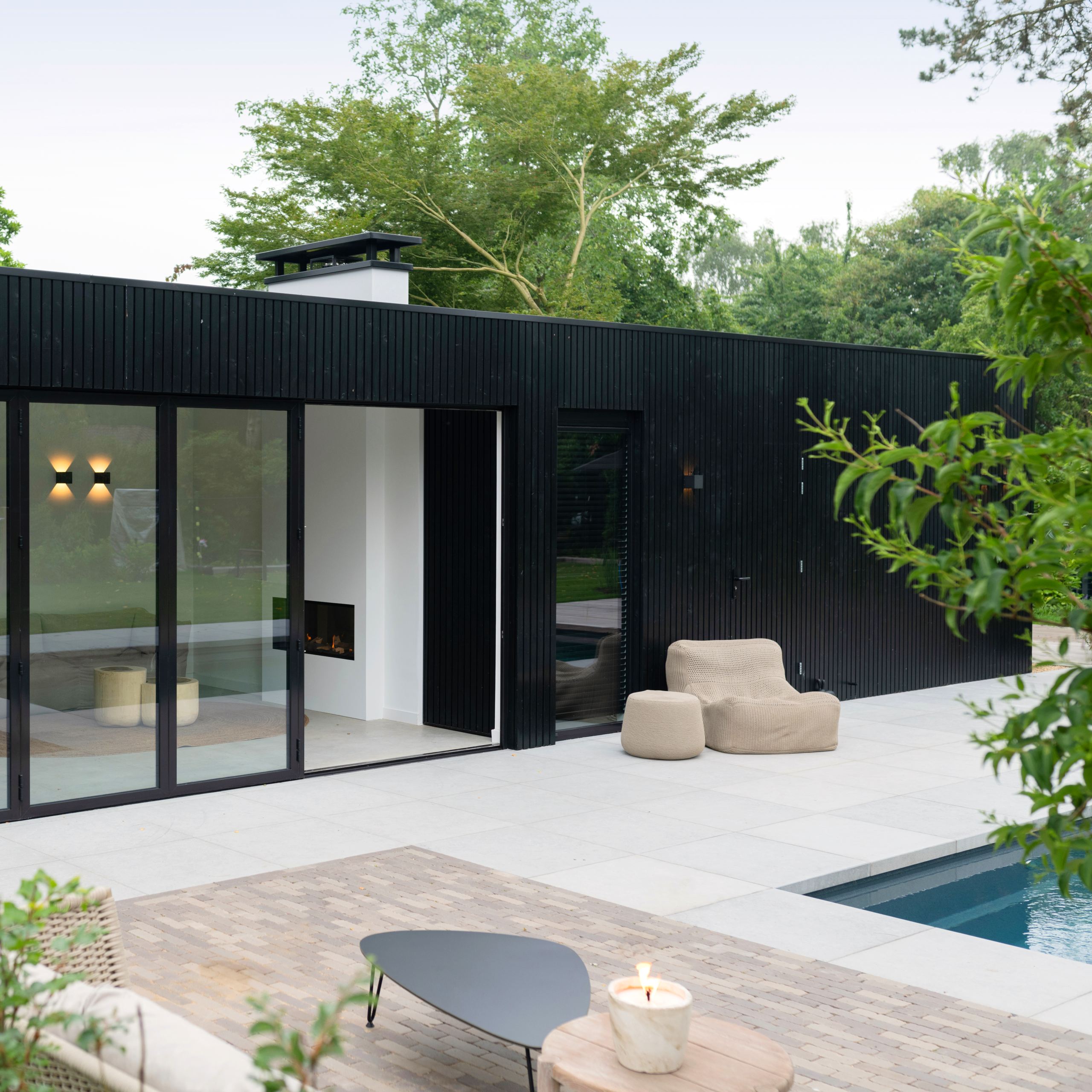 Een zwart poolhouse met rhombus profiel en grote lichtgrijze terrastegels met zwembad