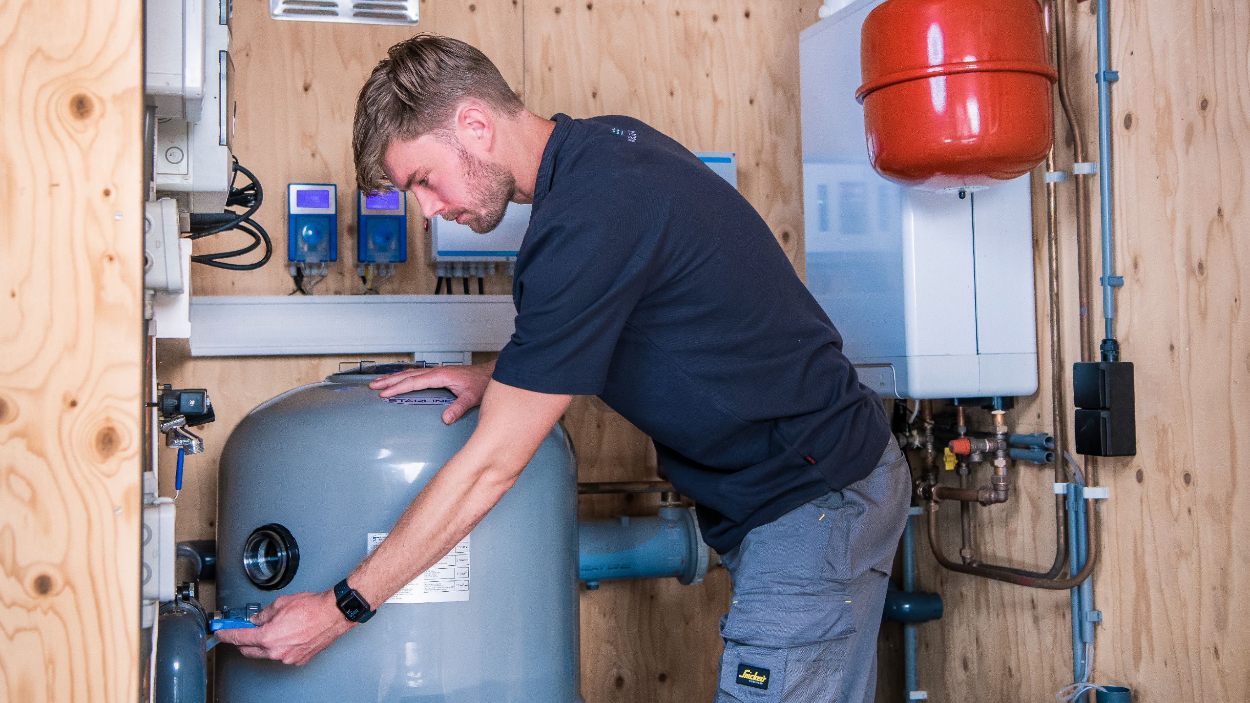 Servicemonteur die werkt bij zwembadfilter in een gehele zwembadtechniek installatieruimte