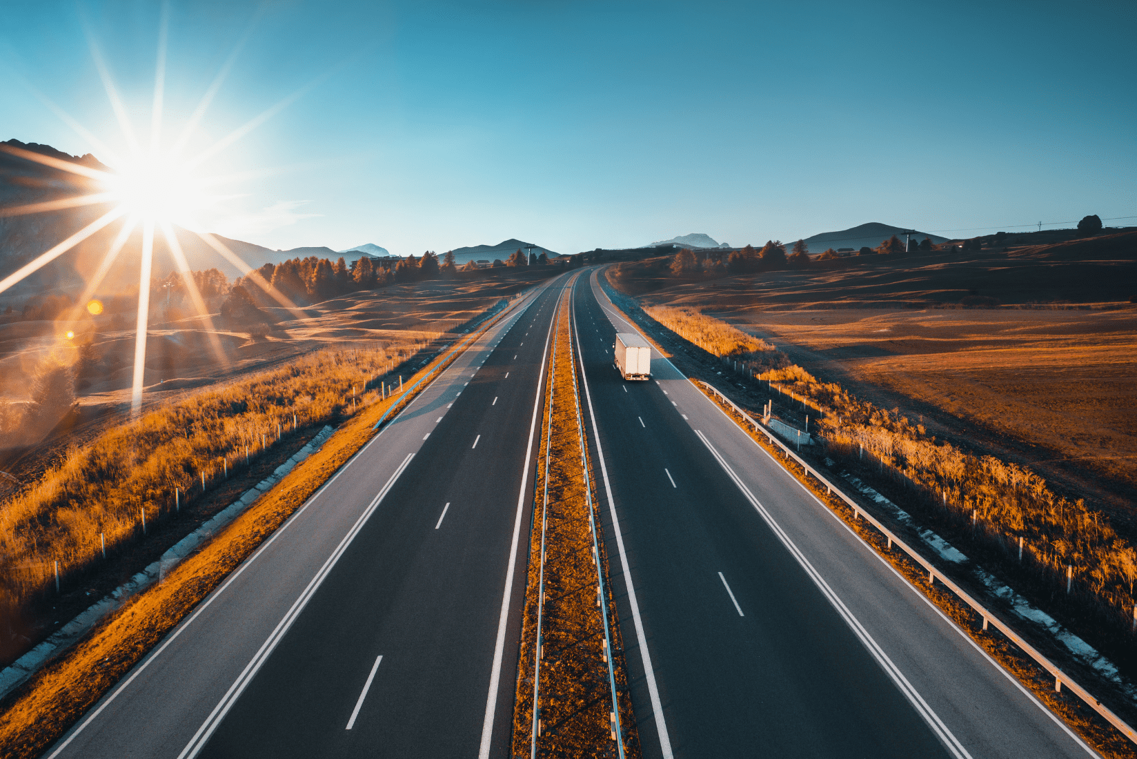 Fotografía de una gran carretera rodeada de naturaleza con un sol poniente de fondo
