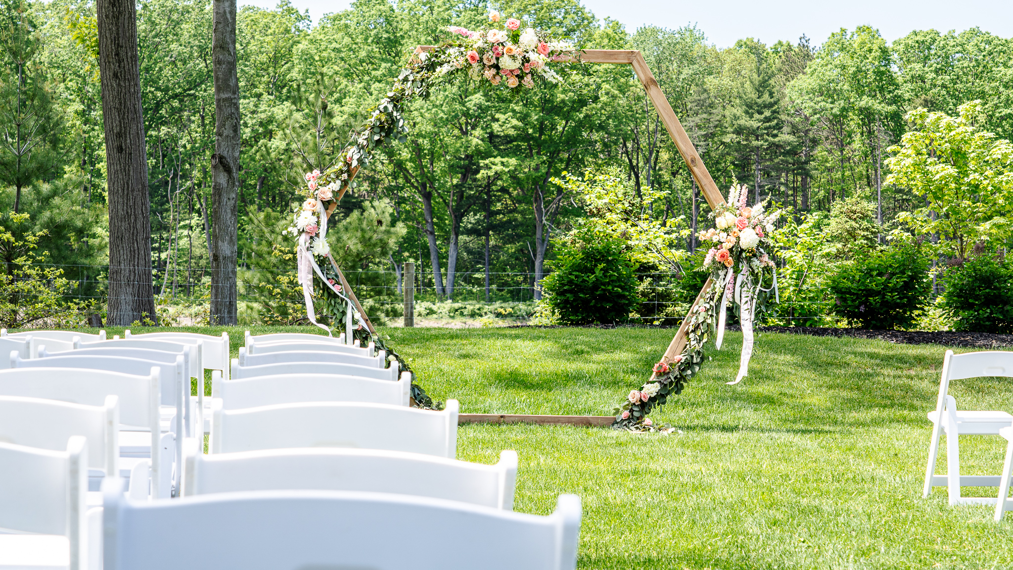A wooden arche covered in flowers and sitting at the front of a arrangement of chairs.
